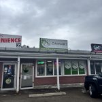 Red-brick cannabis store with green 'KS' logos, a red 'CANNABIS' flag, and a green door marked 'OPEN' at the center entrance.