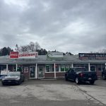 Small plaza with a cannabis store, convenience store, and bar, with cars parked in front under a cloudy sky