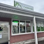 Red-brick cannabis store with green 'KS' logos, a red 'CANNABIS' flag, and a green door marked 'OPEN' at the center entrance.